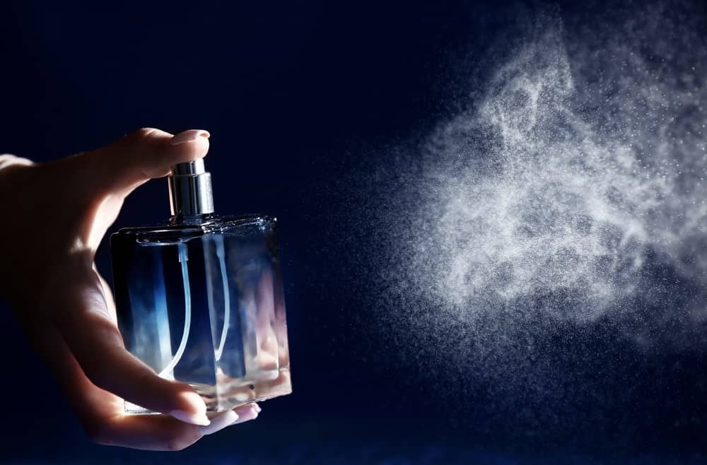 Hand spraying perfume in a cloud of luminous particles against a dark background — BOLD Factory